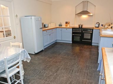 A kitchen with blue cabinets a black stove a blue fridge and a table with chairs at Porthcurno Bay View in Porthcurno