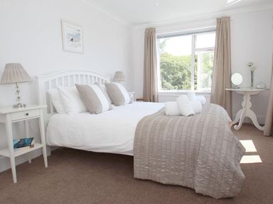 A bedroom with a double bed bedside tables lamps and a window at Porthcurno Bay View in Porthcurno
