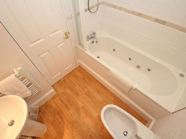 A bathroom with a bathtub shower toilet sink towel rail and wooden floor at Porthcurno Bay View in Porthcurno