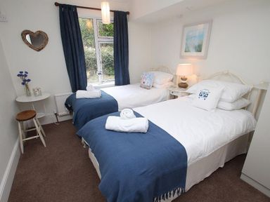 A bedroom with two single beds blue throws and white linens at Porthcurno Bay View in Porthcurno