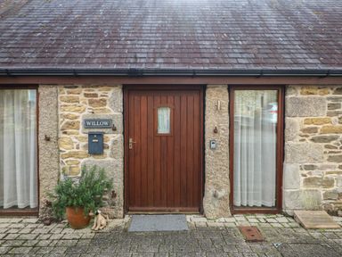 A stone house exterior with a wooden door and two windows with curtains and a plant in a pot at Willow in Falmouth