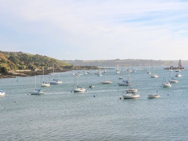 A harbor with multiple sailboats anchored near the shore with hills in the background at Willow in Falmouth