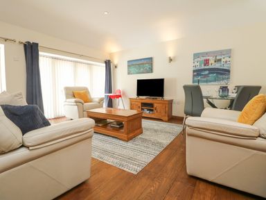A living room with beige sofas a wooden coffee table a television on a wooden stand and a dining table with gray chairs at Willow in Falmouth