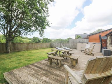 A backyard with a wooden deck table chairs and a picnic bench next to a grass lawn and a wooden fence at Willow in Falmouth
