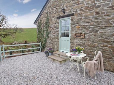 A stone house exterior with a blue door and a small white table with chairs on a gravel surface at Stocks Barn in Looe