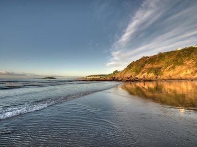 A coastal scene with a sandy beach water waves and a rocky hill at Stocks Barn in Looe