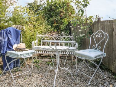 A small outdoor seating area with white metal chairs and a table on a gravel surface at Stocks Barn in Looe