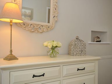 A living room with a lamp and flowers on a chest of drawers at Stocks Barn Looe