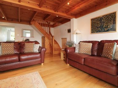 A living room with two brown leather sofas and wooden staircase at Halvosso in Falmouth