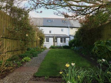 A garden with grass a stone path and flowers bordered by wooden fences at Halvosso in Falmouth