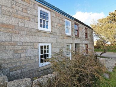 Stone cottage with white and brown window frames and shrubs in front at Halvosso in Falmouth