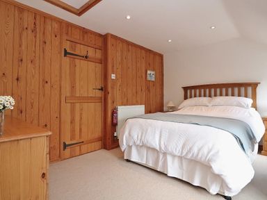 A bedroom with a wooden bed frame a bed with white linens wood paneled walls a wooden door a wooden dresser and a bedside table with a lamp at Halvosso in Falmouth