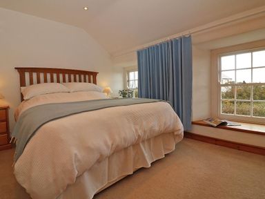A bedroom with a wooden headboard bed, blue curtains, nightstands with lamps and a window ledge with a magazine at Halvosso in Falmouth