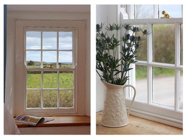 A window with a countryside view and a wooden ledge holding a magazine and a white pitcher with flowers at Halvosso in Falmouth