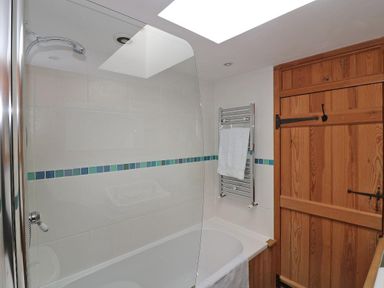 A bathroom with a white bathtub white tiled walls with blue and green tiles a metal towel rack with a white towel and a wooden door at Halvosso in Falmouth