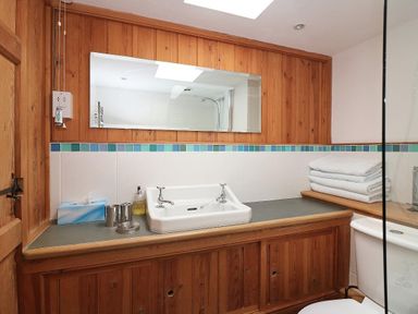 A bathroom with a sink, mirror, stacked towels, and toilet at Halvosso in Falmouth