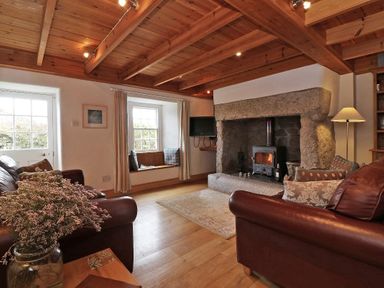 A living room with brown leather sofas a stone fireplace a window seat and wooden ceiling beams at Halvosso in Falmouth