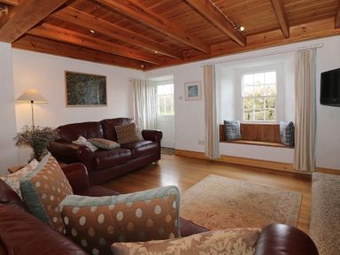 A living room with leather sofas cushions a floor lamp a window seat and a wall mounted television at Halvosso in Falmouth
