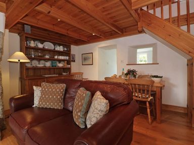 A room with a brown leather sofa with cushions a wooden dining table with chairs a wooden cabinet with dishes and a wooden staircase at Halvosso in Falmouth