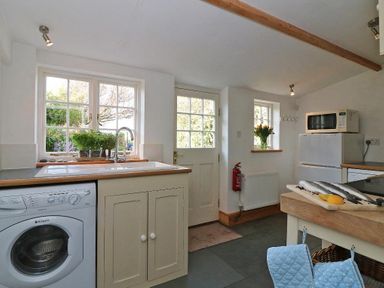 A kitchen with a washing machine under the counter and a sink under a window at Halvosso in Falmouth