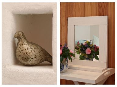 A metallic bird sculpture in a white wall niche and a flower arrangement in a blue and white vase reflected in a small white framed mirror on a wooden wall at Halvosso in Falmouth