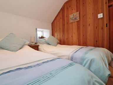 A bedroom with two single beds a wooden wall a small window and a bedside table with a lamp at Halvosso in Falmouth