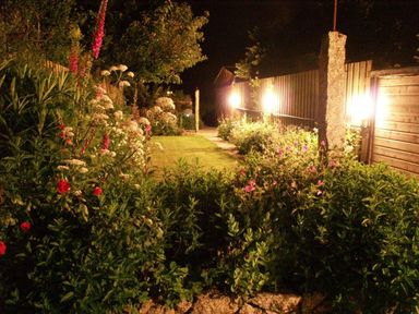 A garden at night with flowers bushes grass and fence lights at Halvosso in Falmouth