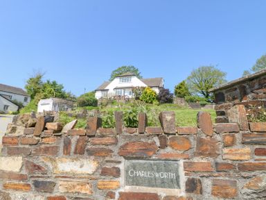 A brick wall with a nameplate reading Charlesworth and a white house with gardens behind it at Charlesworth in Braunton