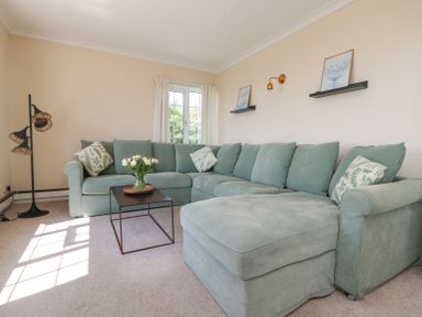 A living room with a green sectional sofa a black floor lamp and a small table with flowers at Charlesworth in Braunton