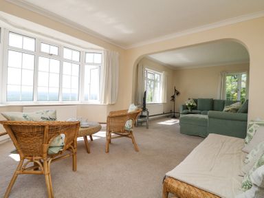 A living room with wicker chairs and a round table near large windows and a green sofa set at Charlesworth in Braunton