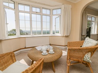 A room with wicker chairs and a wicker table set near large bay windows at Charlesworth in Braunton