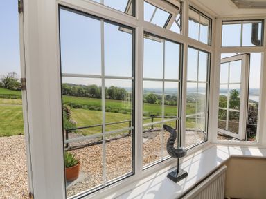 A bay window with an ornamental object on the sill overlooking a garden and countryside at Charlesworth in Braunton