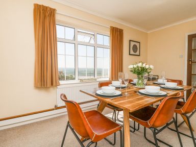 A dining room with a wooden table set for six and orange chairs near a window at Charlesworth in Braunton