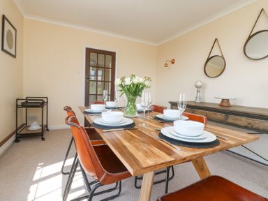 A dining room with a wooden table set for six with brown chairs and a sideboard with mirrors at Charlesworth in Braunton