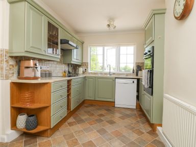 A kitchen with green cabinets white appliances and a window at Charlesworth in Braunton