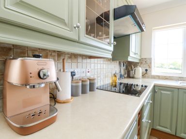 A kitchen countertop with a coffee machine paper towel holder canisters stovetop and window at Charlesworth in Braunton