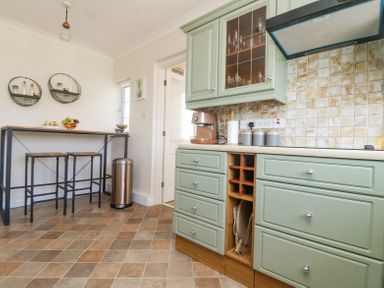 A kitchen with green cabinets a wooden table with stools and a trash bin at Charlesworth in Braunton