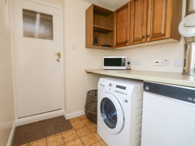 A utility room with a washing machine microwave wooden cabinets and a door at Charlesworth in Braunton