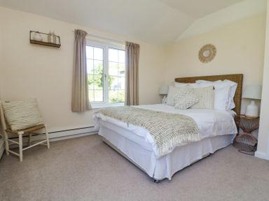 A bedroom with a bed pillows lamps a chair and a window at Charlesworth Braunton
