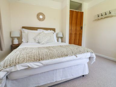 A bedroom with a bed with pillows and blankets two lamps wooden door and wall hooks at Charlesworth in Braunton