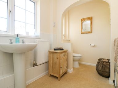 A bathroom with a pedestal sink wooden cabinet and a toilet under an archway at Charlesworth in Braunton