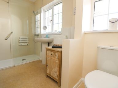 A bathroom with a shower area a sink a wooden cabinet towels and a toilet at Charlesworth in Braunton