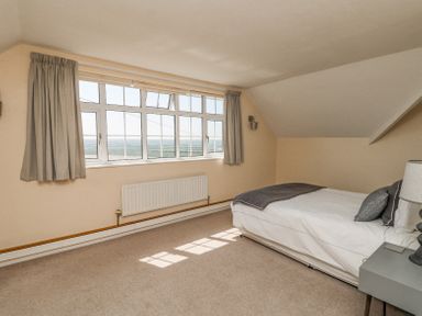 A bedroom with a bed side table lamp radiator and a large window with curtains at Charlesworth in Braunton