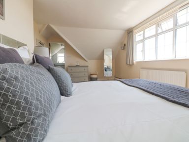 A bedroom with a large bed with cushions a chest of drawers a standing mirror and a window at Charlesworth in Braunton