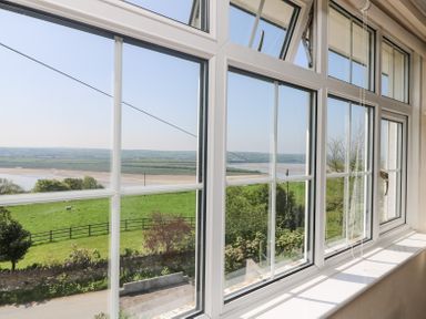 A window with white frames overlooking a green field a fence and a river beyond at Charlesworth in Braunton