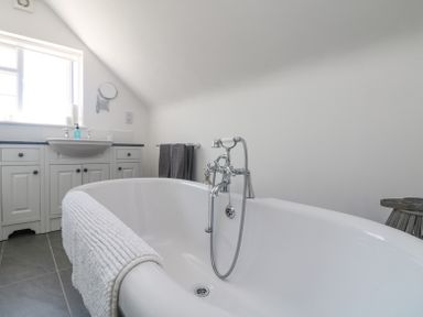 A bathroom with a white bathtub and a sink under a window at Charlesworth in Braunton