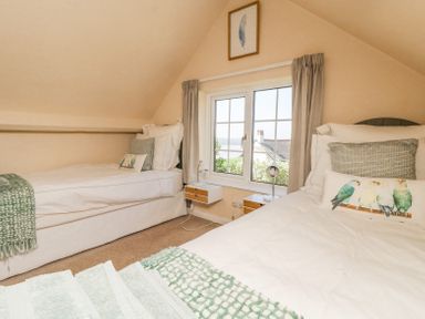 A bedroom with two single beds separated by a window with curtains at Charlesworth in Braunton