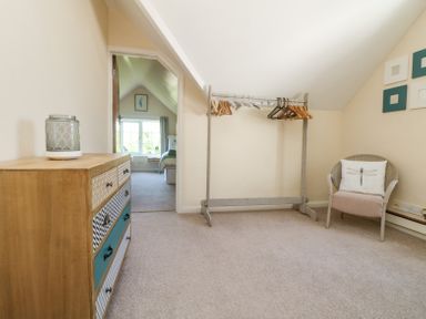 A room with a wooden dresser a standing clothes rack with hangers and a chair with a pillow at Charlesworth in Braunton