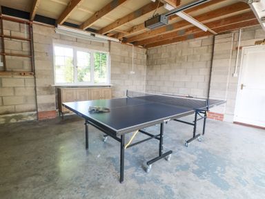 A table tennis table with paddles and a ball in a garage with a window a white door and exposed wooden ceiling beams at Charlesworth in Braunton