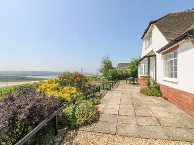 An outdoor patio area next to a house with plants and a railing overlooking fields and water at Charlesworth in Braunton